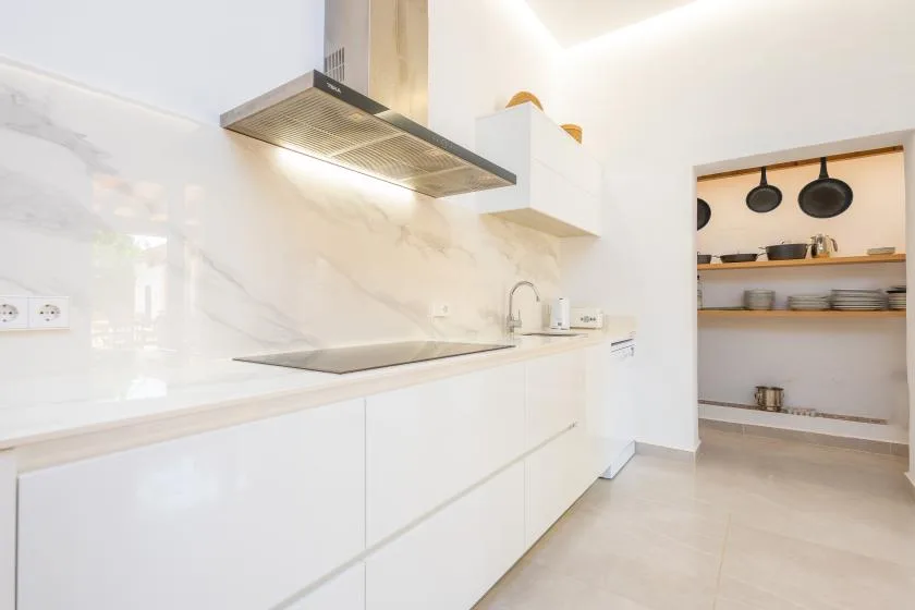 Una cocina moderna y luminosa con gabinetes blancos, una placa de cocina y estantes abiertos.