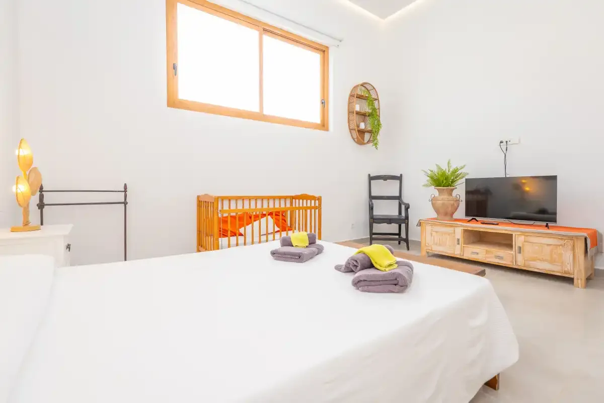 Un dormitorio luminoso con una cama, una cuna de madera y un televisor.