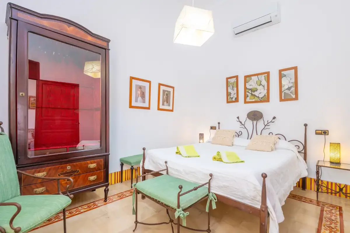 Un dormitorio con una cama blanca, cuadros enmarcados y un gran armario de madera oscura.