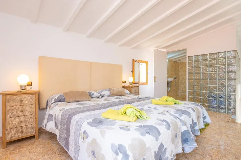 Un dormitorio con ropa de cama estampada, muebles junto a la cama y un tabique de bloques de vidrio.