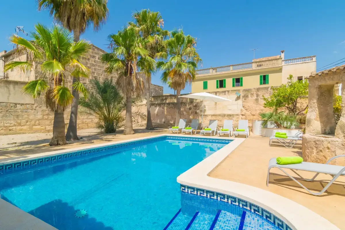 Una piscina al aire libre está junto a un patio de piedra soleado con palmeras.