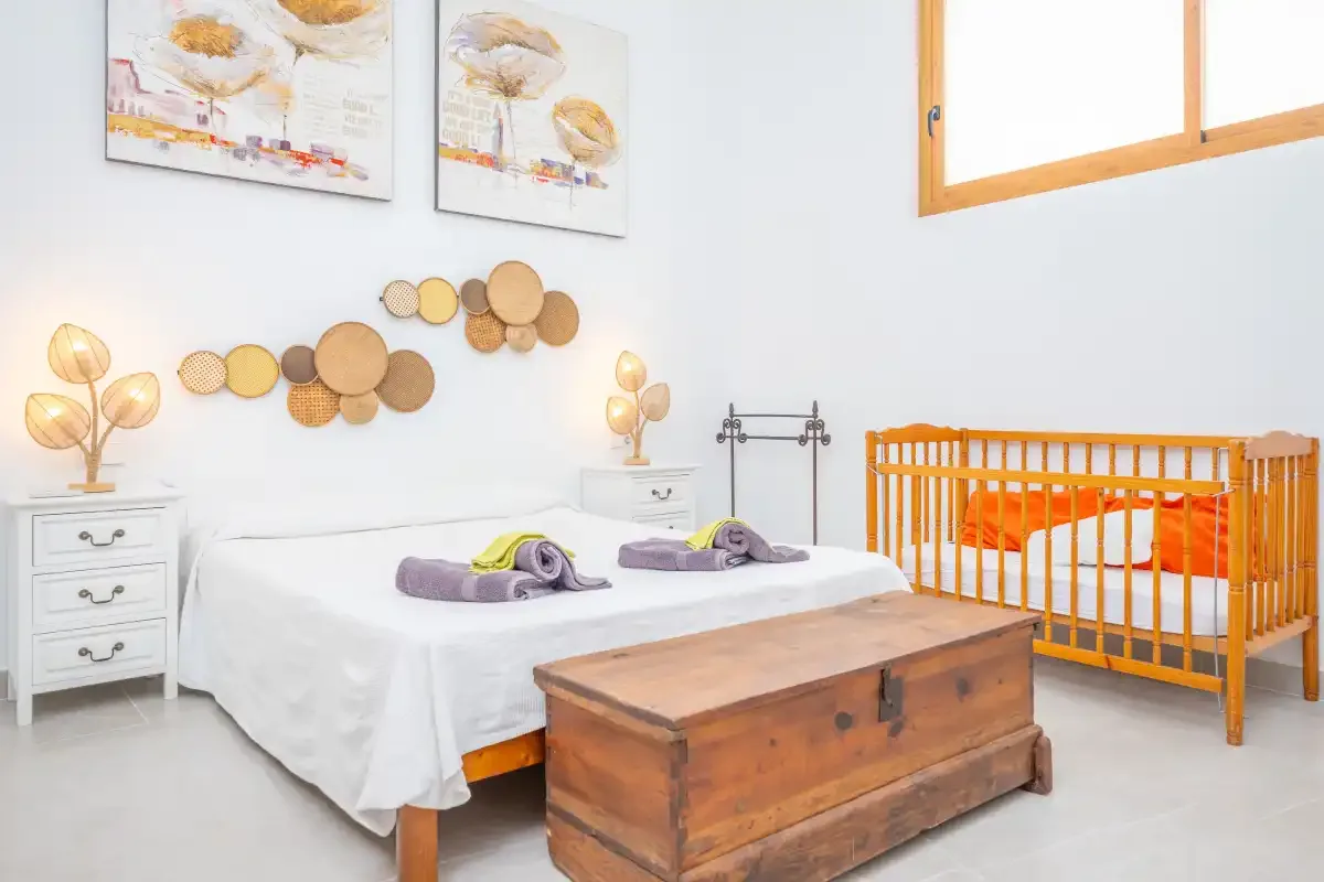 Un dormitorio luminoso con una cama, un arcón de madera y una cuna naranja.