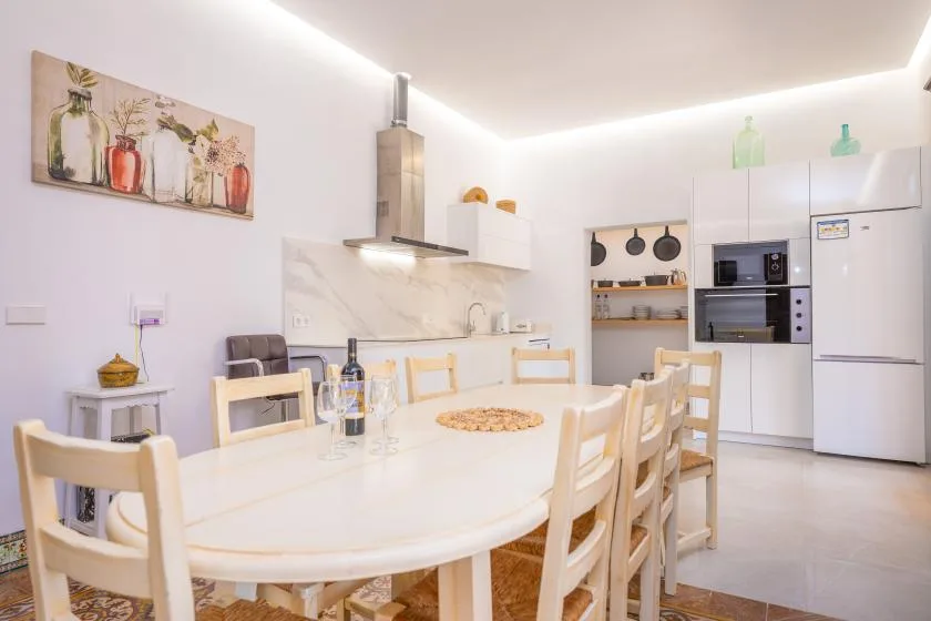 Una cocina y comedor luminosos con una mesa larga y asientos de tonos claros.