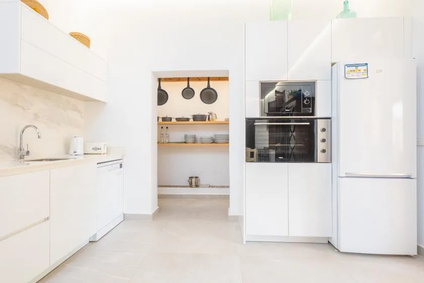 Una cocina blanca y luminosa con electrodomésticos empotrados y estantes abiertos con utensilios.