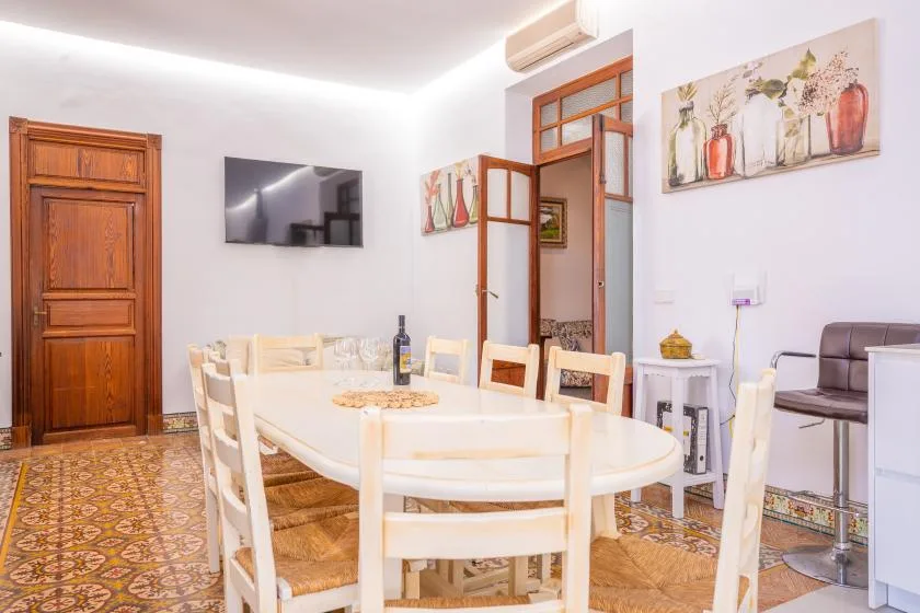 Comedor con mesa y sillas blancas, suelo de baldosas estampadas y cuadros en la pared.