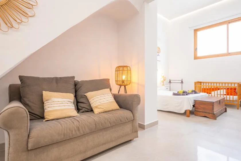 Un dormitorio luminoso con un sofá gris, una cama y una cuna naranja.