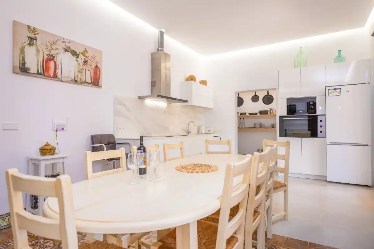 Una cocina y comedor luminosos con una mesa larga y electrodomésticos integrados.