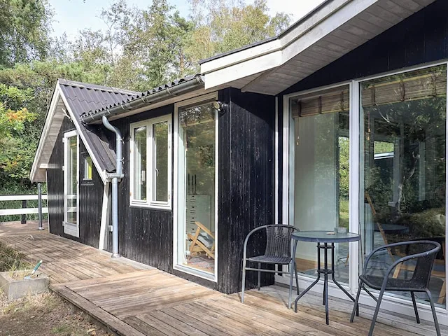 Una casa de revestimiento oscuro da a una terraza de madera con asientos al aire libre.