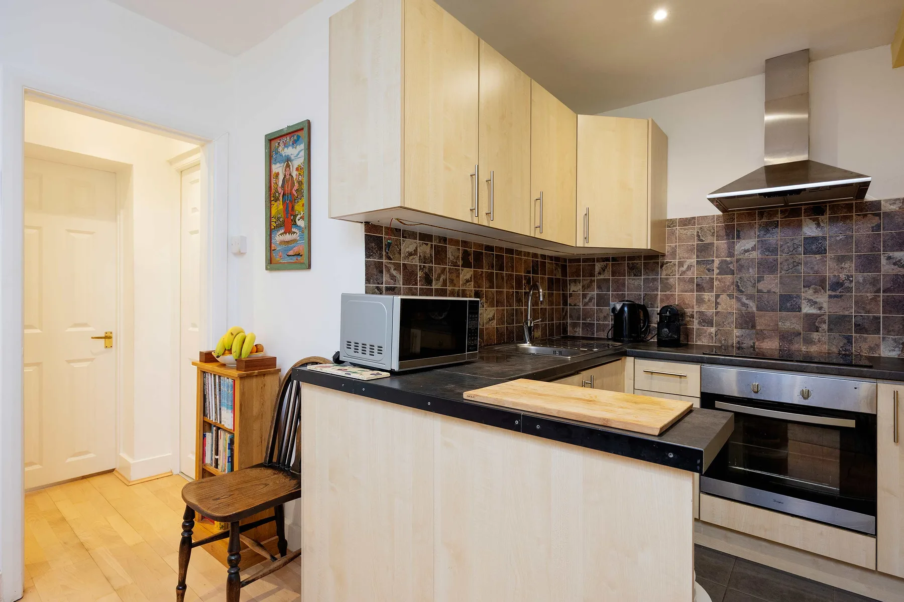 A compact kitchen with light cabinetry, dark countertops, and a built-in oven.