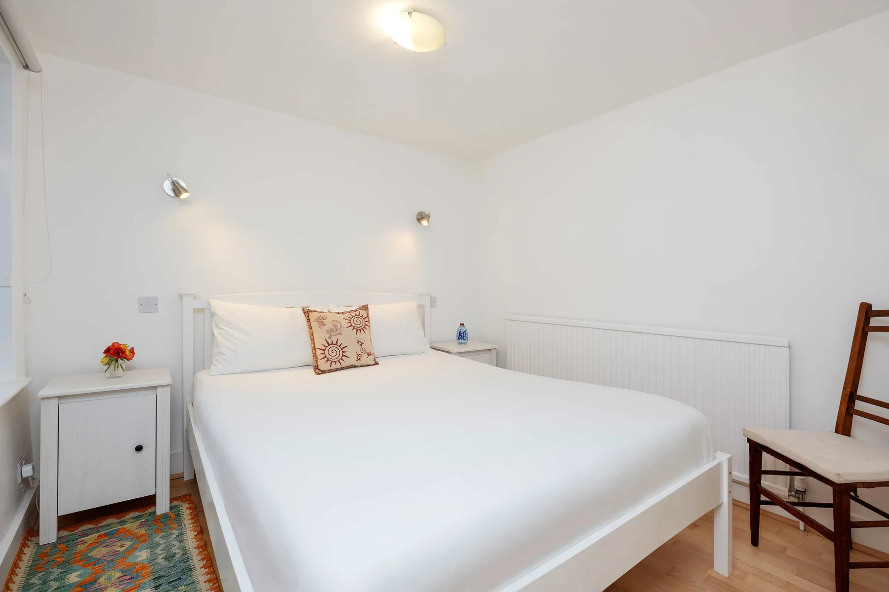 A bright bedroom with a neatly made bed and a chair beside it.