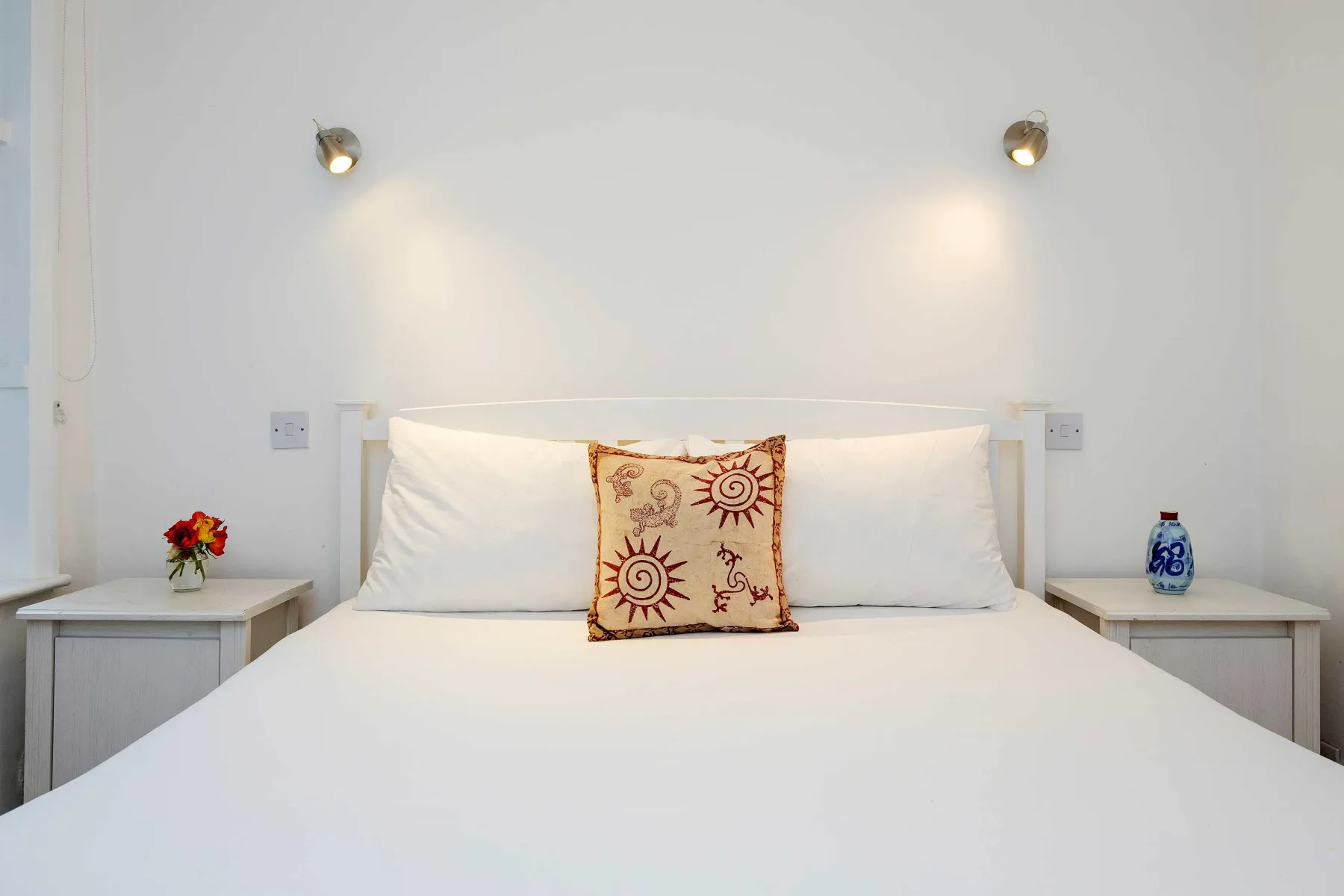 A neatly made bed with white bedding and a patterned accent pillow.
