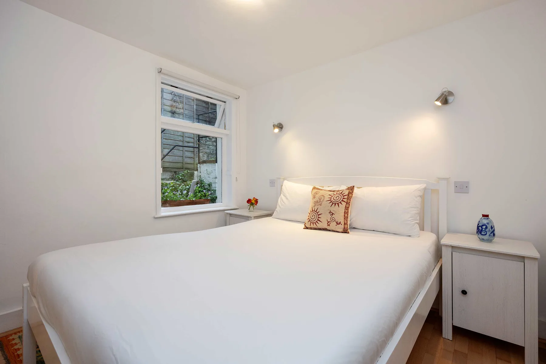 A bright bedroom with a white bed, decorative cushion, and bedside table.