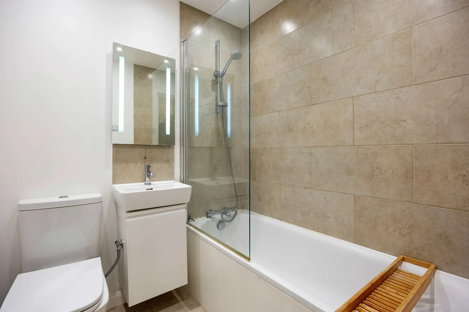 A bathroom with a bathtub, glass shower screen, sink, and toilet.
