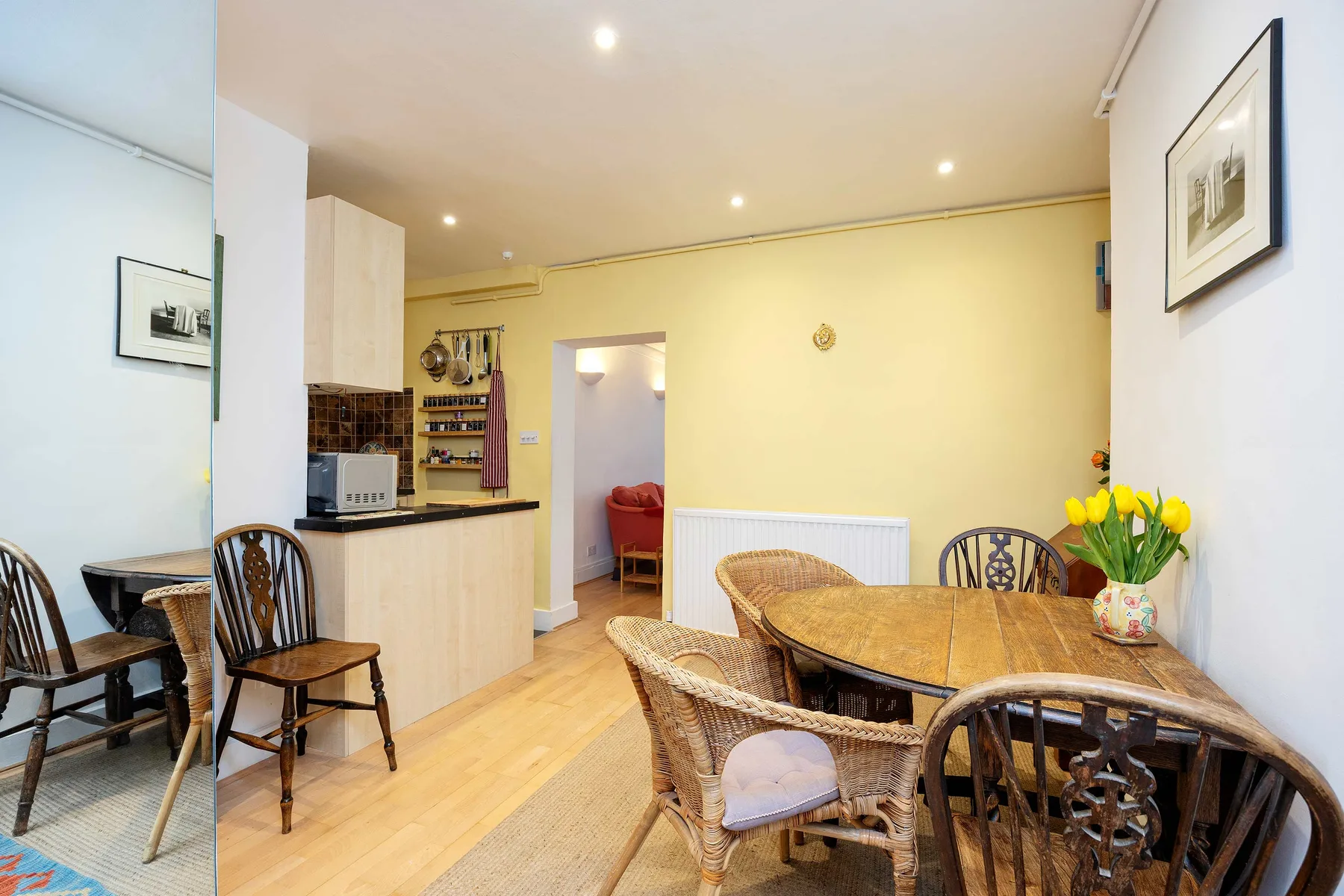 A dining area with a wooden table and wicker seating beside a compact kitchen.