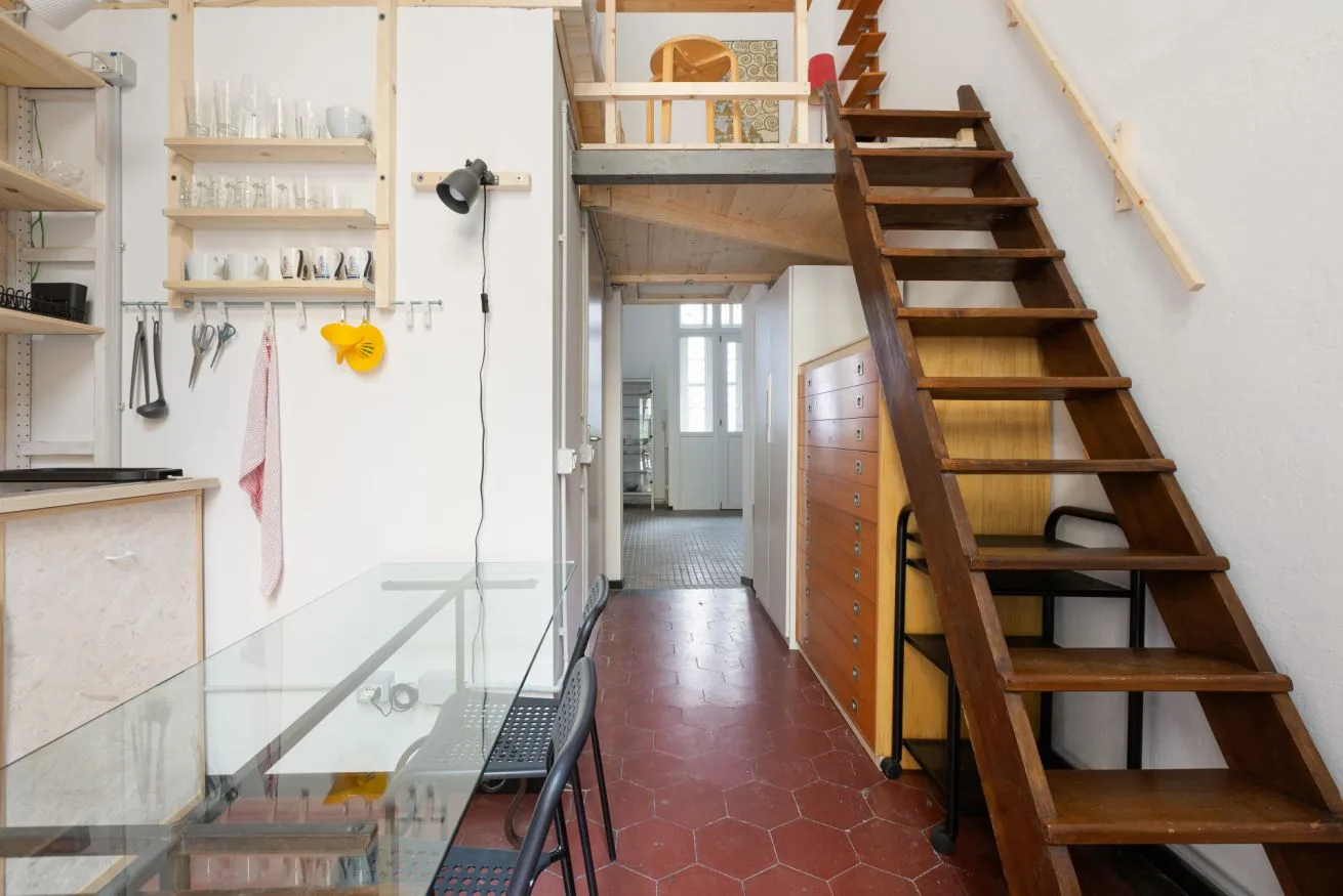 Un interior compacto con una zona de cocina y una escalera de madera que conduce a un altillo.