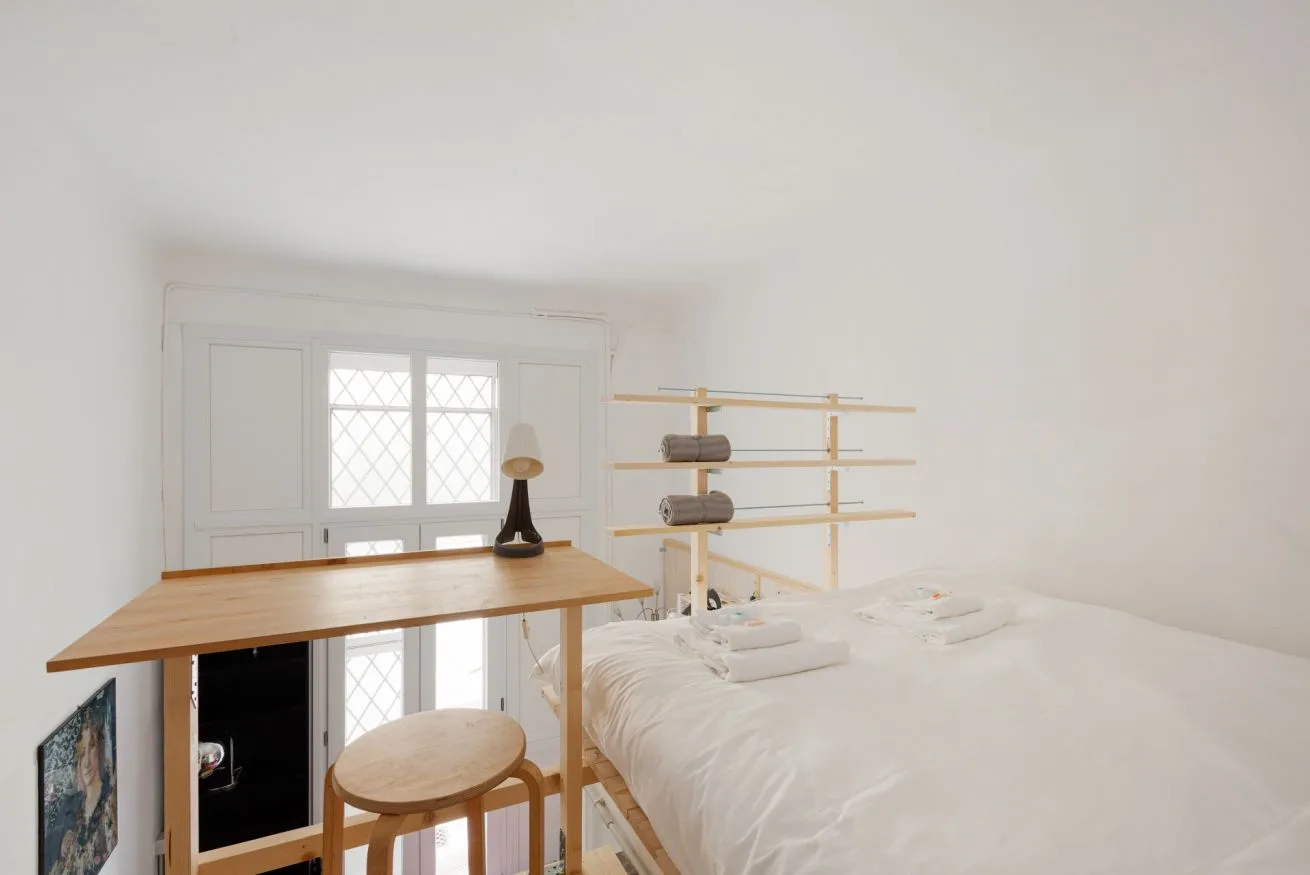 Un dormitorio luminoso con una cama, un escritorio de madera y estantes en la pared.