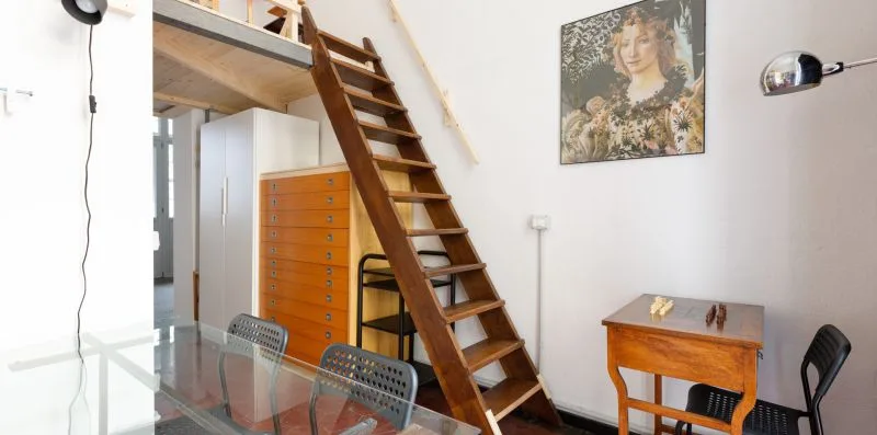 Un comedor con una mesa de vidrio junto a una escalera de madera y armarios.