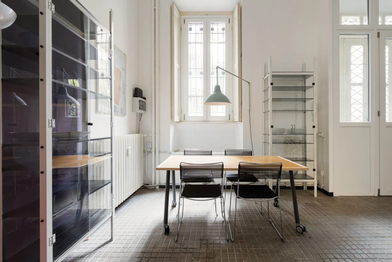 Un comedor luminoso con una mesa y sillas junto a ventanas altas.