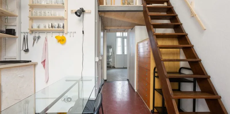 Una cocina estrecha y un pasillo con una escalera de madera y una mesa de vidrio.
