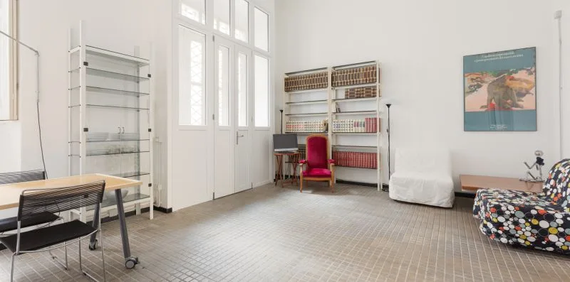 Una habitación luminosa con ventanas altas, estanterías, un escritorio y asientos.