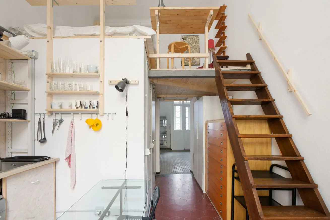 Un interior compacto tipo loft con una escalera de madera junto a una zona elevada para dormir.