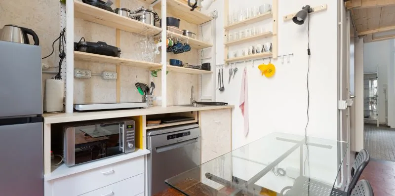 Una cocina con estantes abiertos, electrodomésticos sobre la encimera y una mesa de vidrio.