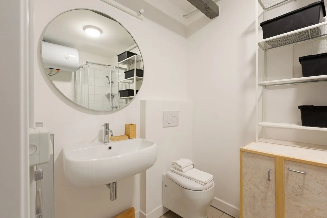 Un baño con lavabo de pared, inodoro y estantes de almacenamiento.