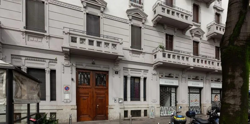 Un edificio blanco de varias plantas con balcones, locales y una entrada de madera.