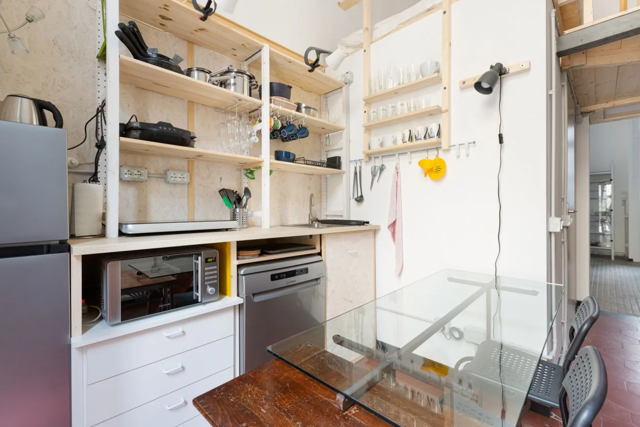 Una cocina con estantes abiertos, electrodomésticos sobre la encimera y una mesa de vidrio.