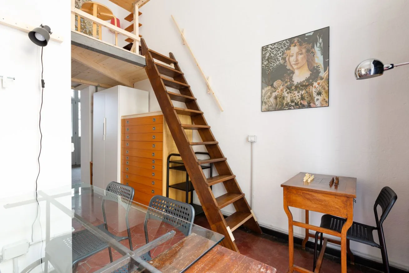 Una luminosa habitación tipo loft con una escalera de madera hacia una zona elevada para dormir.