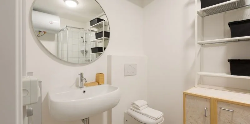 Un baño luminoso con lavabo, inodoro y espejo redondo en la pared.