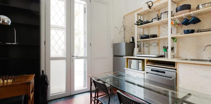 Una cocina luminosa con estantes abiertos, electrodomésticos y una mesa de cristal.