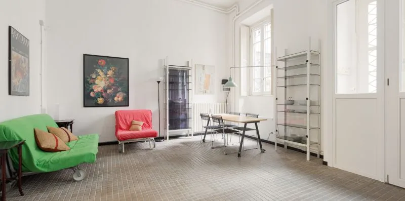 Una habitación luminosa con un sofá verde y una mesa junto a ventanas altas.