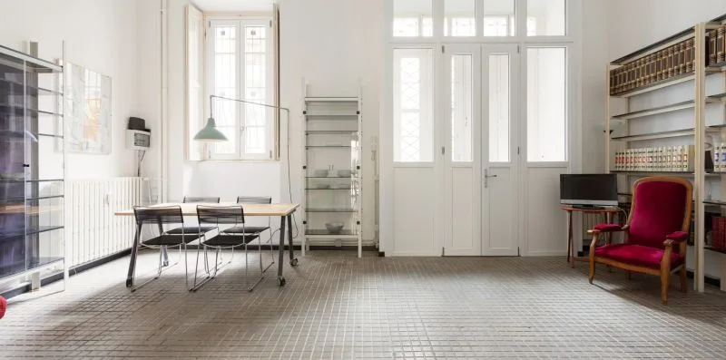 Una sala luminosa con grandes ventanas, una mesa y asientos.
