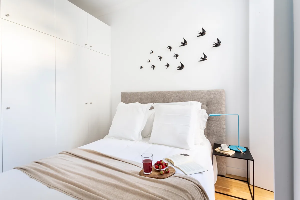 A bright bedroom with a neatly made bed and bird decorations on the wall.