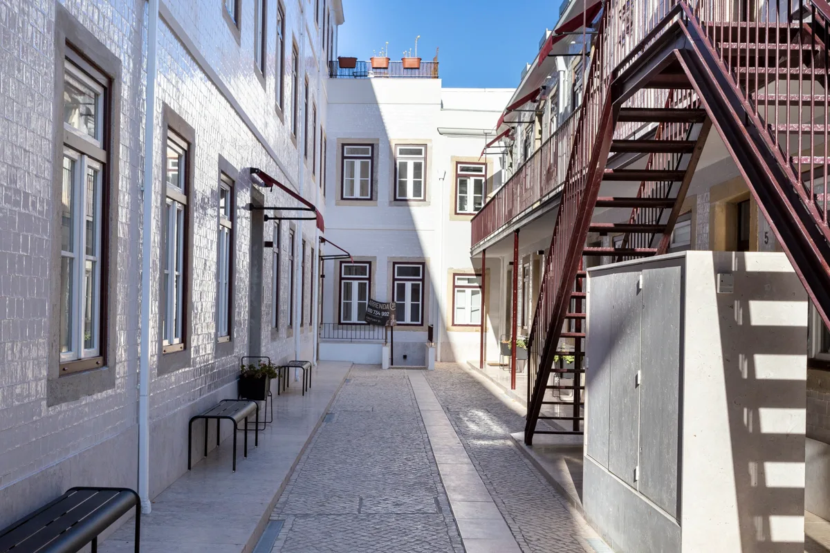 A paved courtyard runs between white buildings, with an exterior staircase along one side.