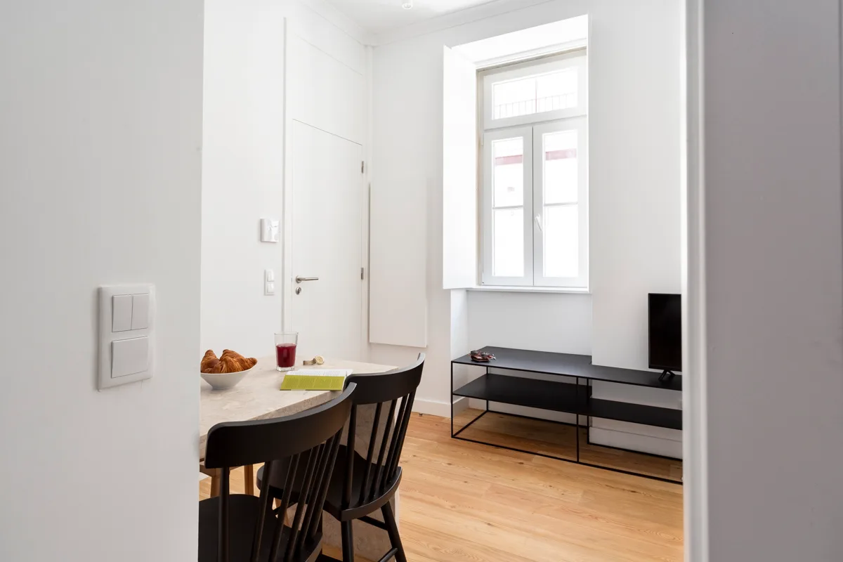 A bright dining area with dark seating beside a window and low media stand.