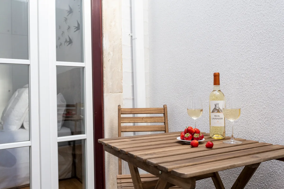 A small outdoor dining area with a wooden table set with wine and strawberries.