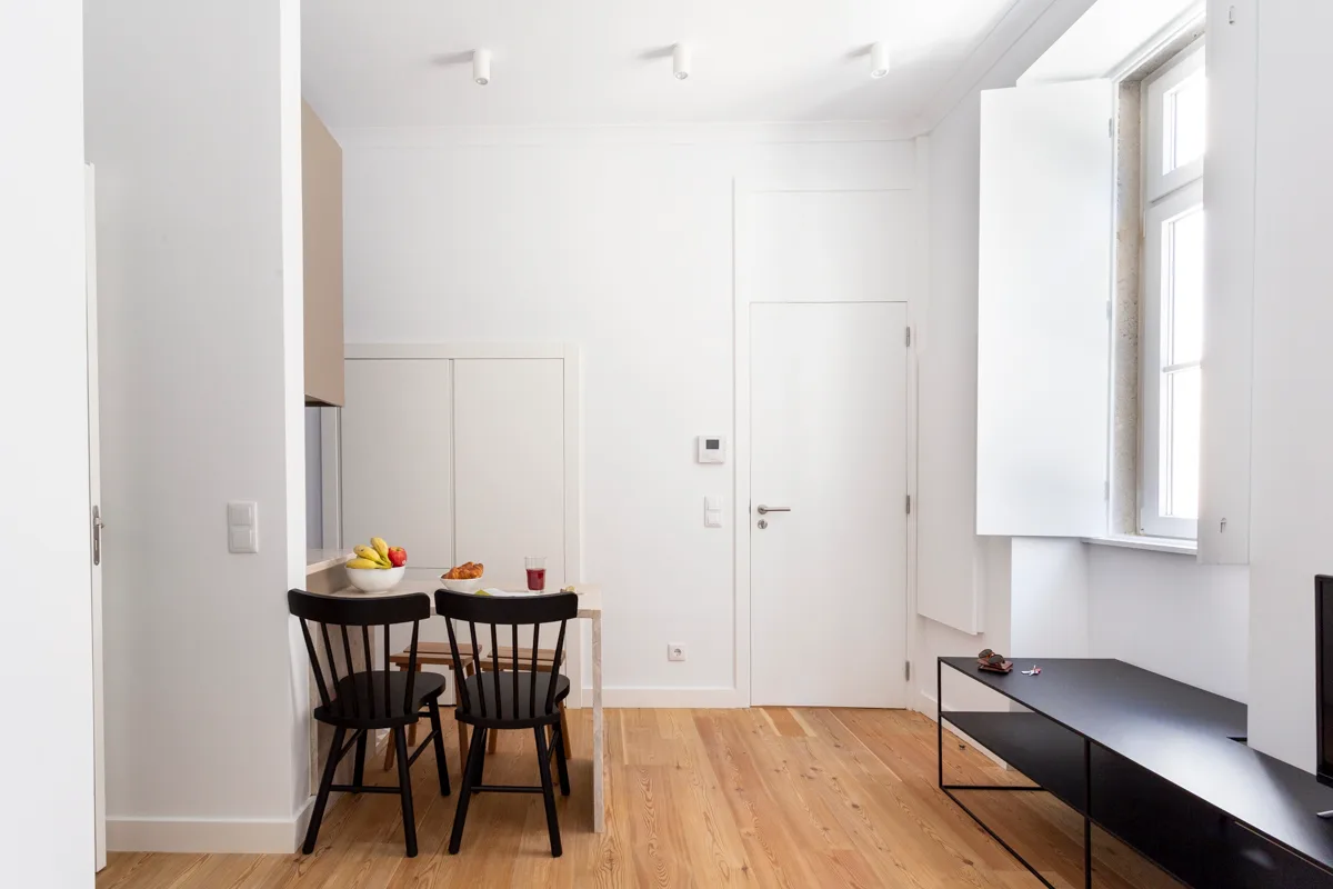 A bright living and dining area with a wooden table and black seating.