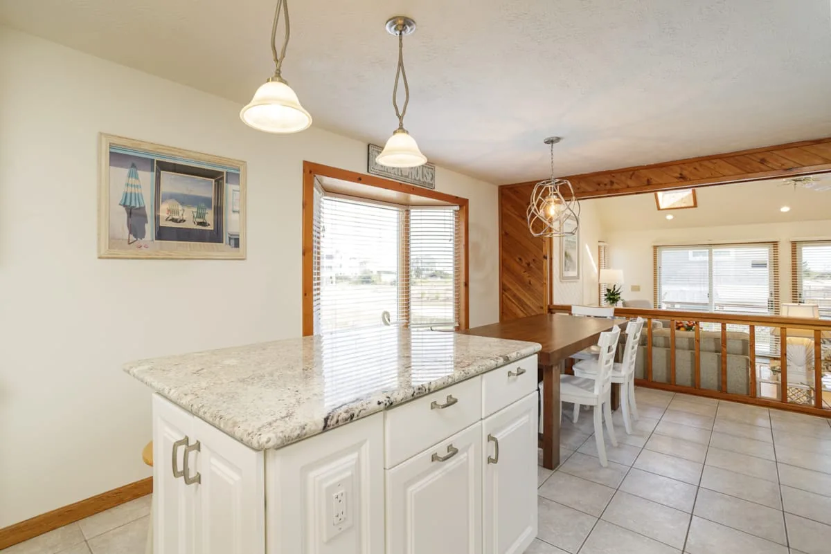 Una cocina luminosa con una isla grande y un comedor al fondo.