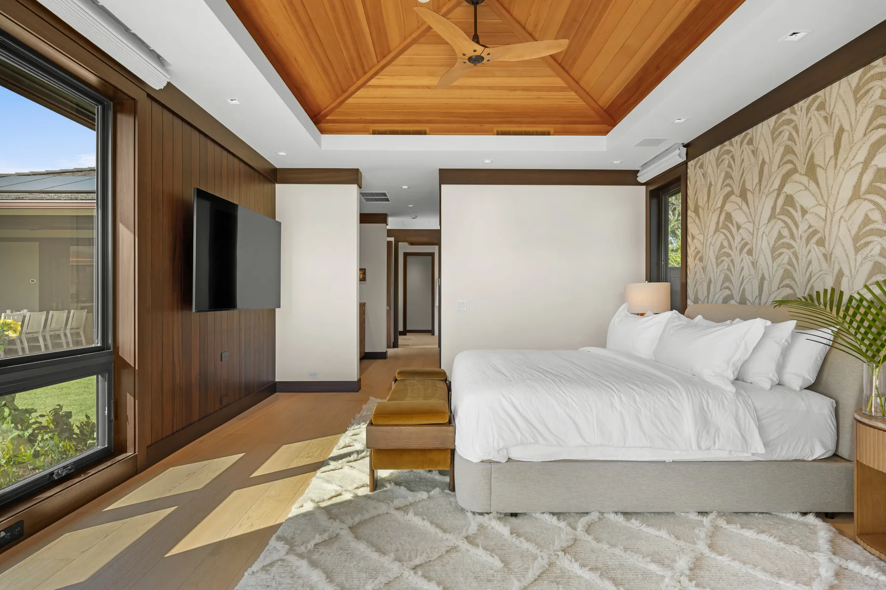 Un dormitorio luminoso con una cama grande, techo de madera y ventanas.