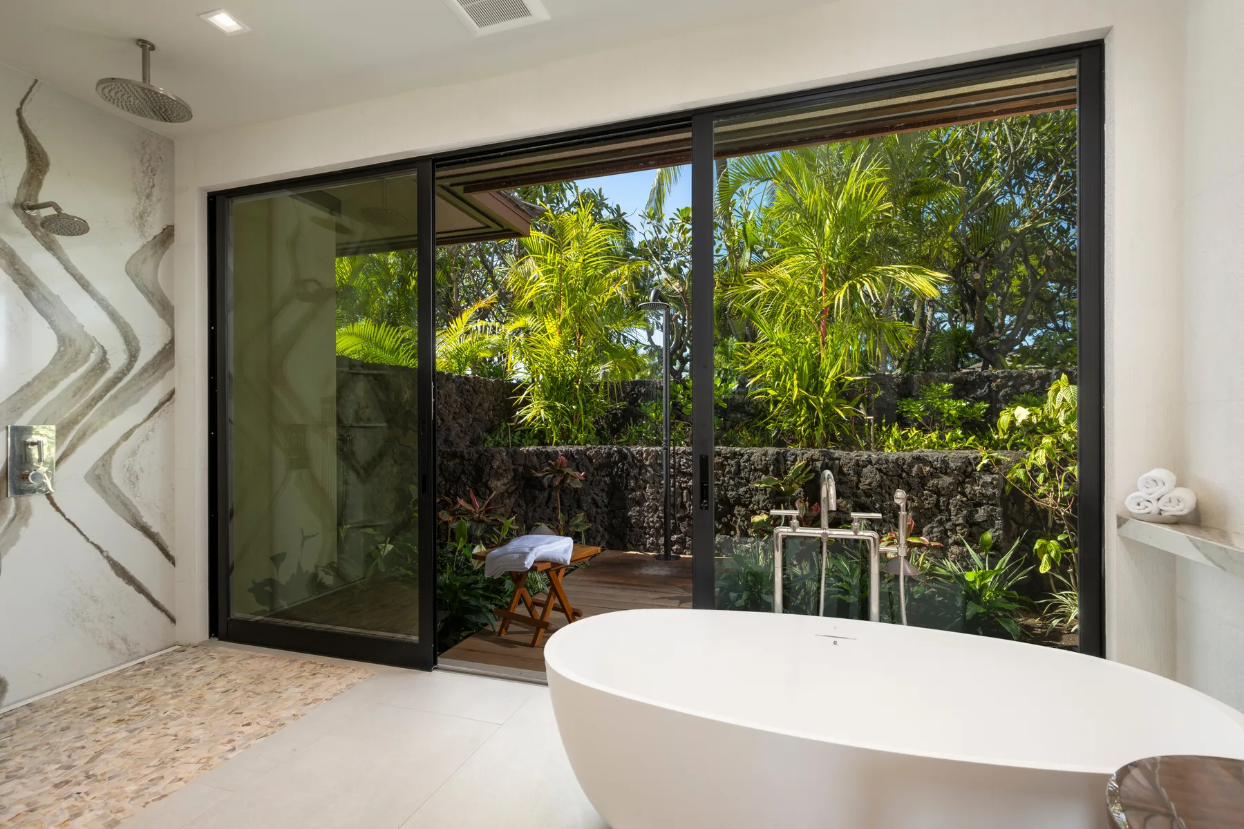 Un baño con una bañera exenta junto a grandes puertas de vidrio con vistas a la vegetación.