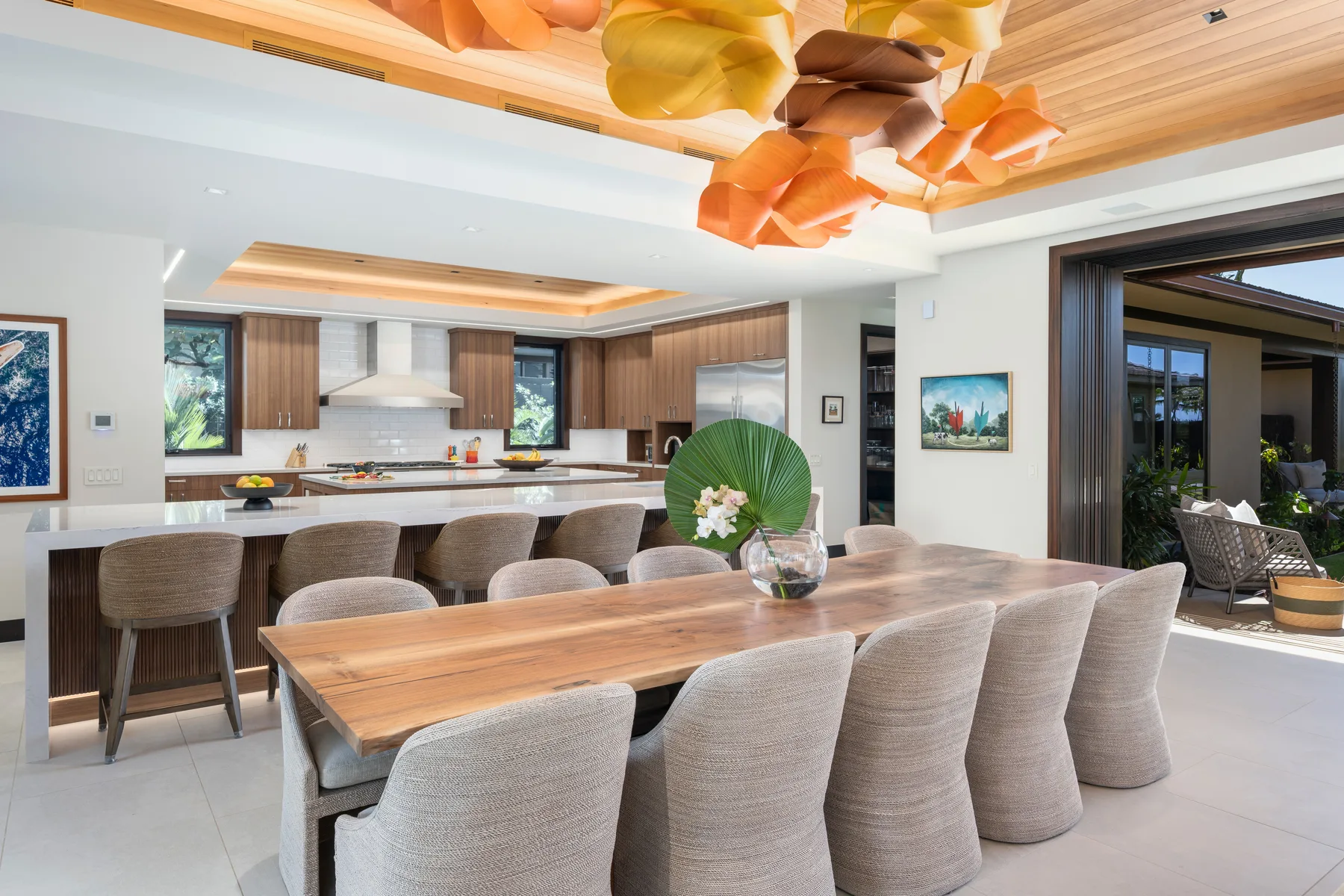 Un comedor moderno tiene una larga mesa de madera y asientos tapizados junto a una cocina abierta.