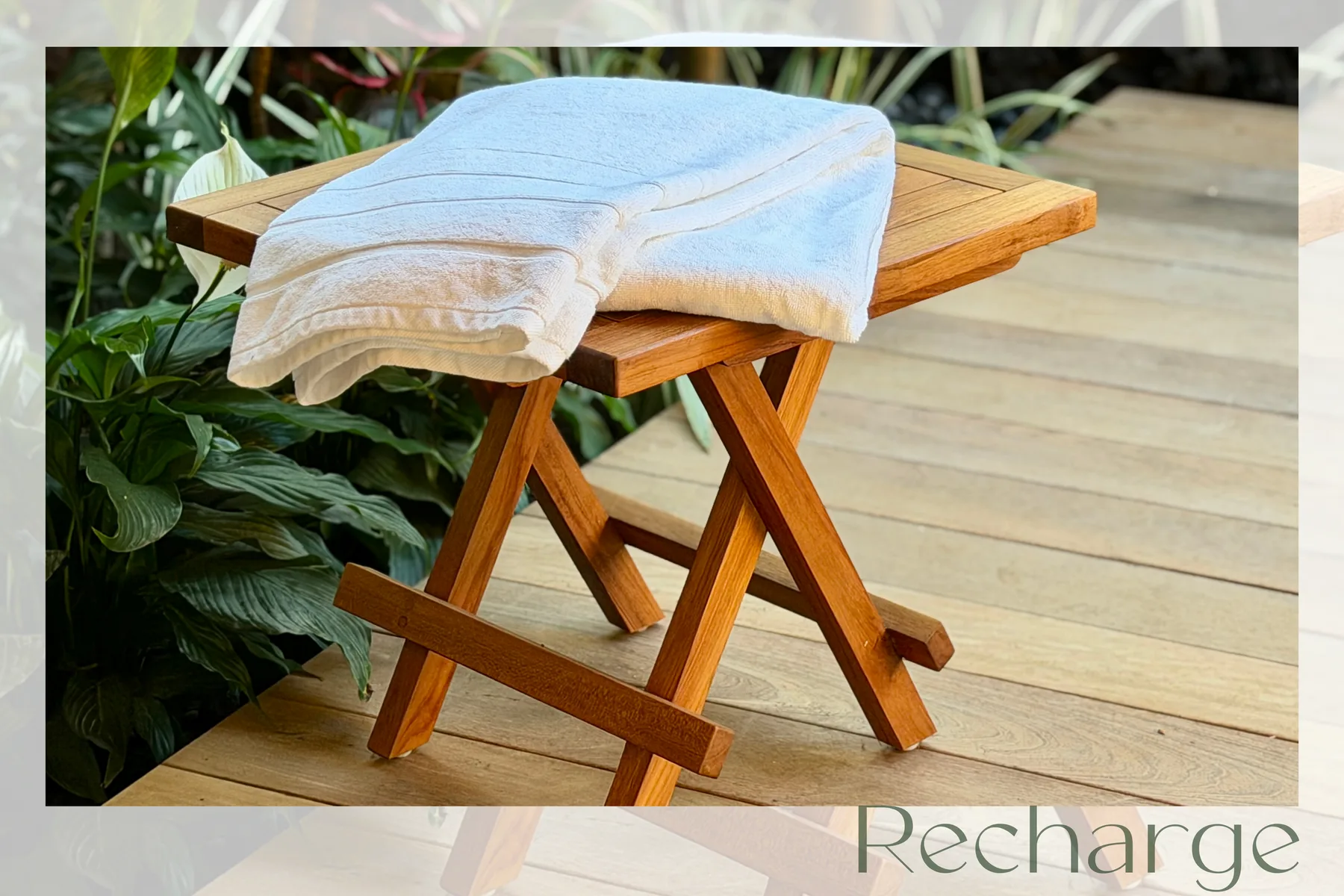 Una mesa pequeña de madera sostiene toallas dobladas junto a plantas frondosas en una terraza.