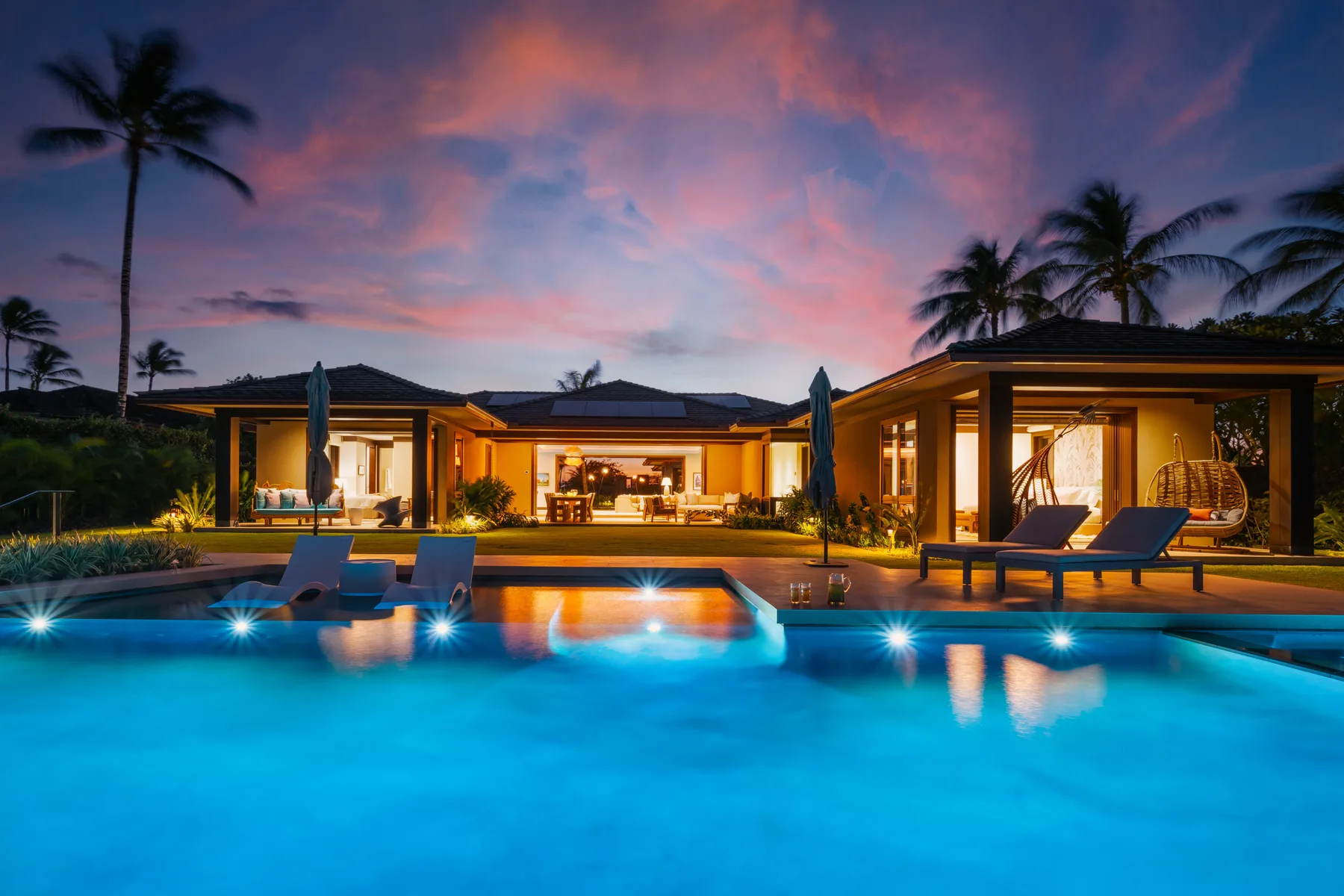 Una villa moderna brilla junto a una piscina bajo un cielo vespertino colorido.