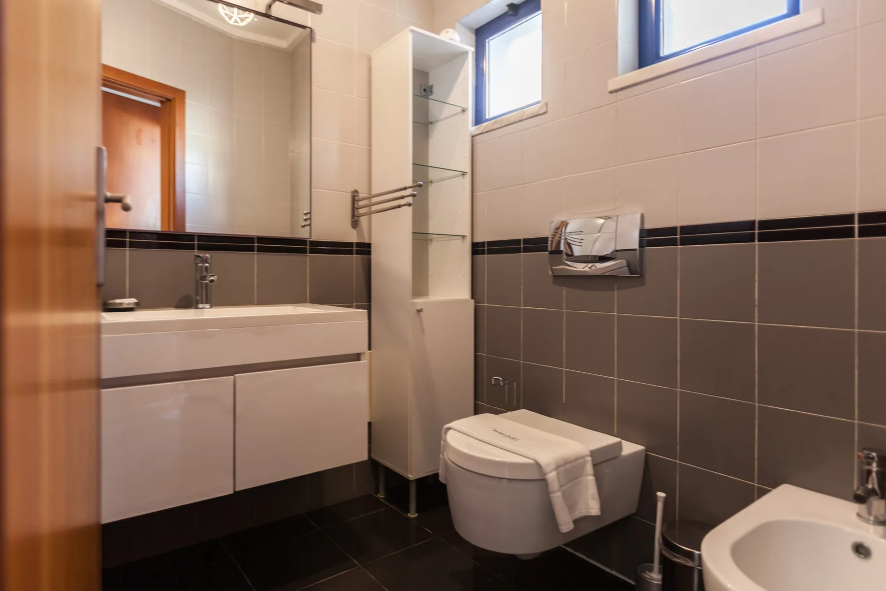 A tiled bathroom with a vanity, wall-mounted toilet, and bidet.