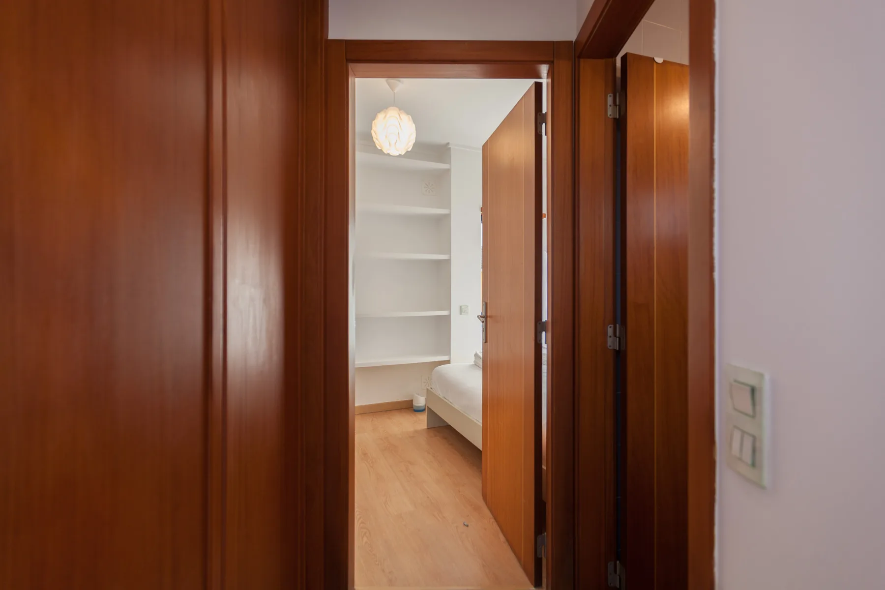 A wood-paneled hallway opens into a bright bedroom with built-in shelves.
