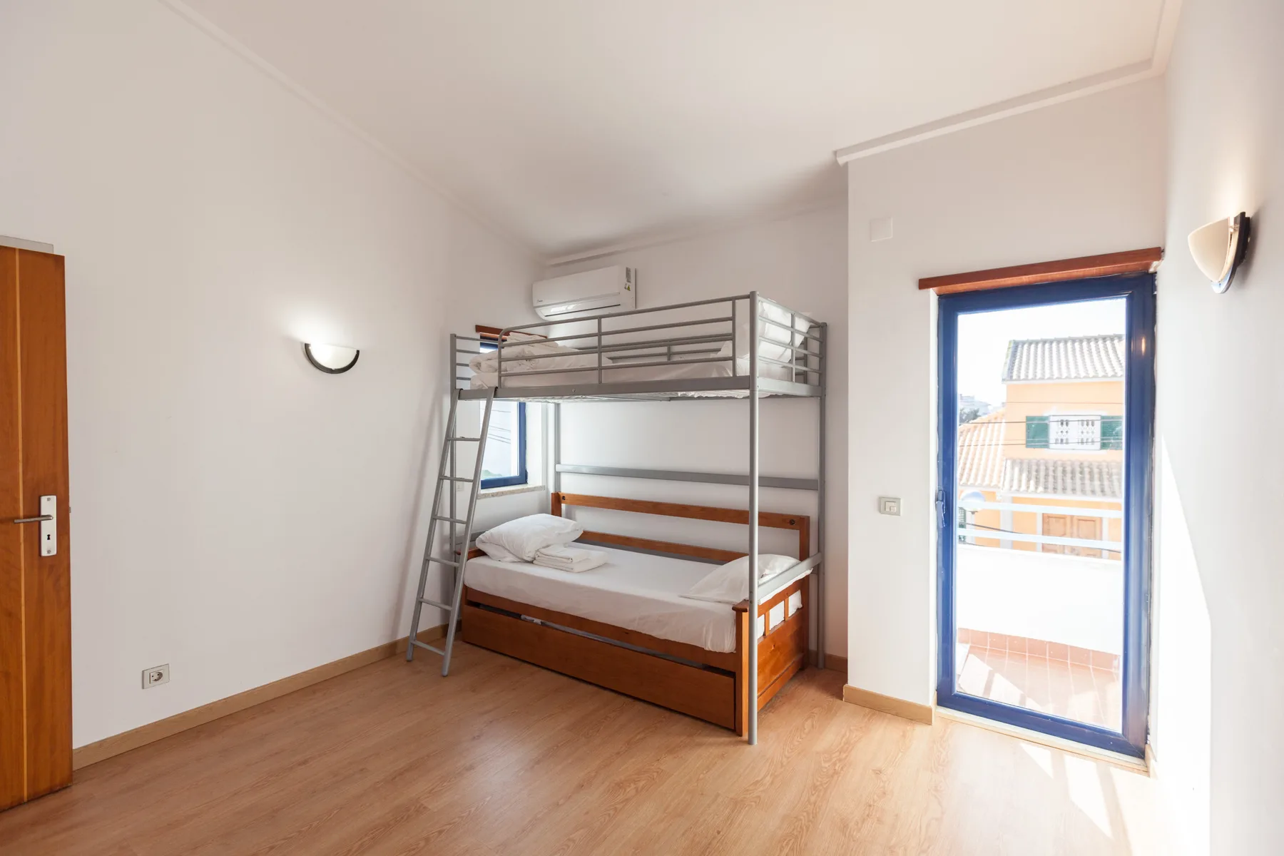 A bedroom with a wooden bunk bed and a bright balcony doorway.
