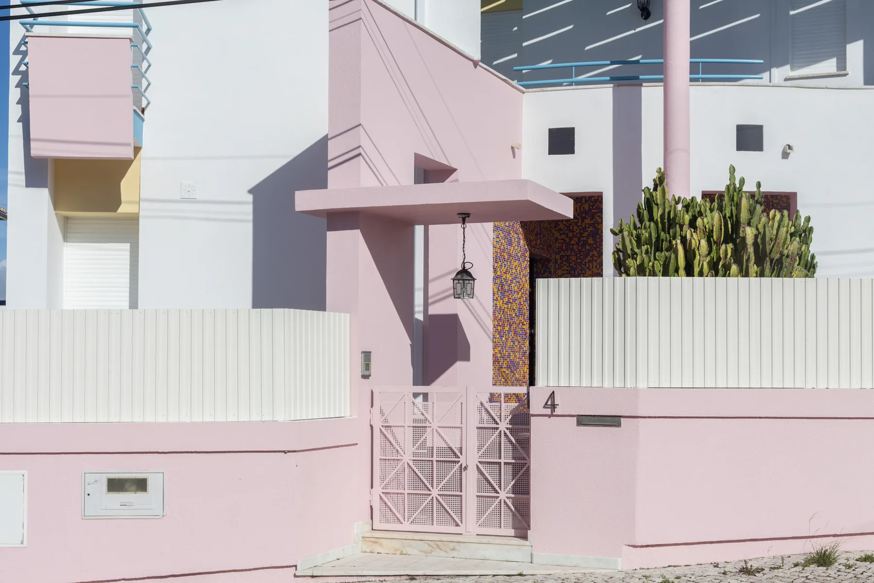 A pink house entrance with a metal gate and a cactus garden.