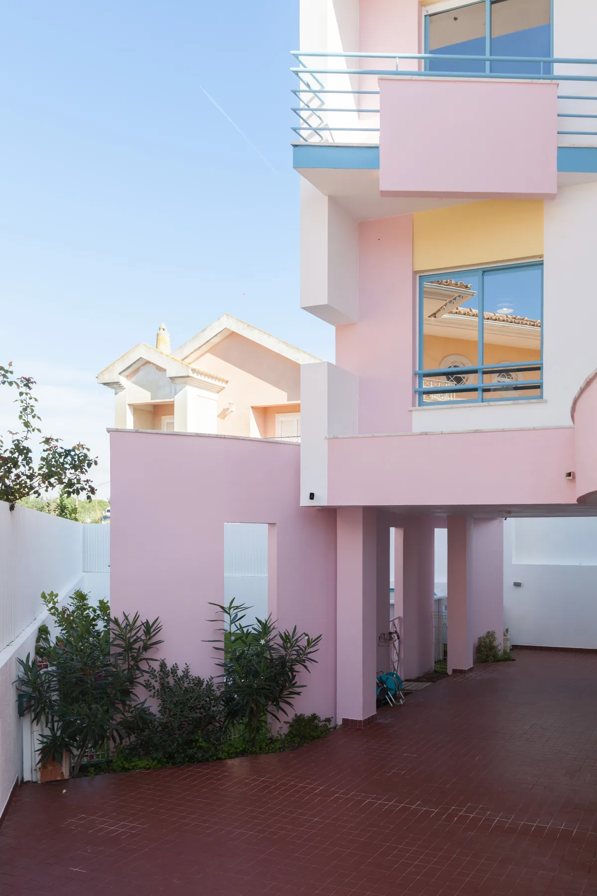 Pink residential buildings surround a paved courtyard with plants and balconies.